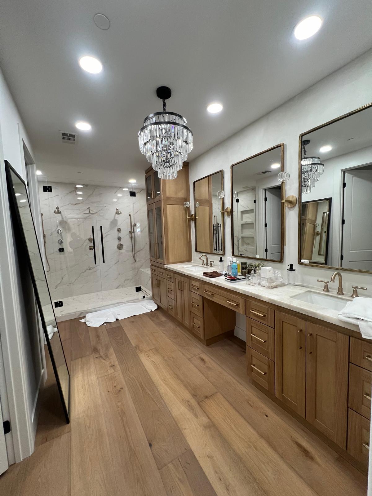 Custom double vanity remodel with white oak cabinetry, marble counters and crystal chandelier